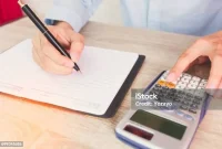 bing_panduan_memilih_kpr_terbaik_untuk_pembelian_rumah_modern_anda_4 Orang menulis catatan keuangan di buku dengan pensil, kalkulator di samping