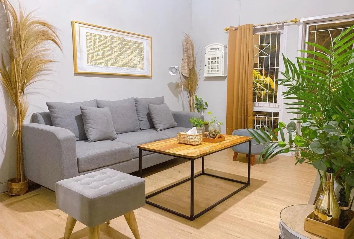 Interior rumah modern dengan ruang tamu terbuka, sofa abu-abu, meja kayu, dan tanaman hias di sudut ruangan