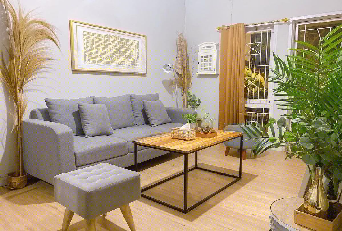 Ruang tamu modern dengan sofa abu-abu, tanaman hijau, dan pencahayaan alami dari jendela besar